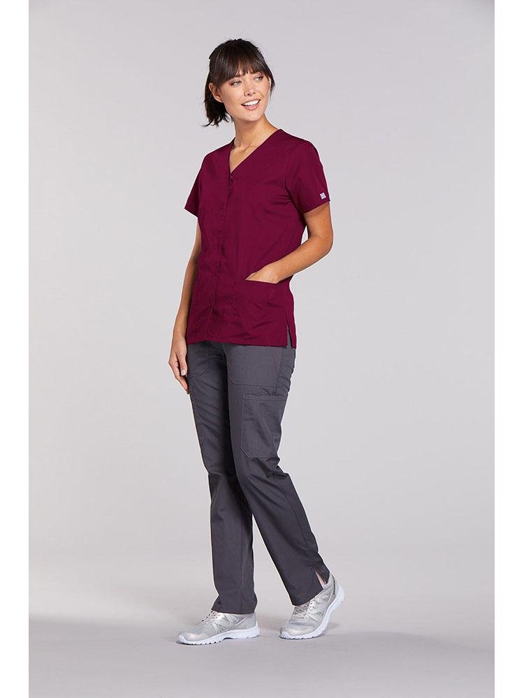 A female Physical Therapist wearing a Cherokee Workwear Originals Women's Snap Front Solid Scrub Top in Wine  size XL featuring side slots for additional range of motion throughout the day.