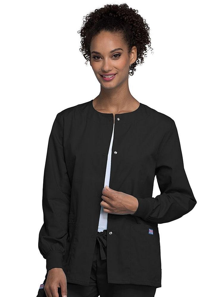 A young female LPN wearing a Cherokee Workwear Originals Women's Snap Front Warm-Up Jacket in black featuring A Traditional Classic fit & a round neck.
