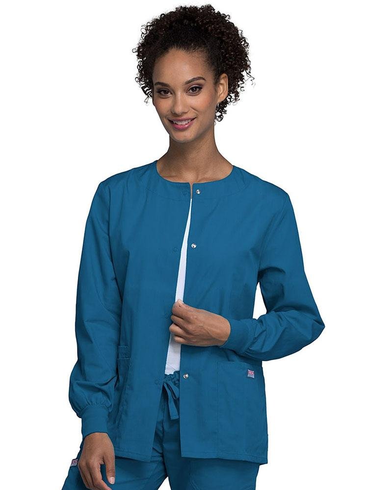 A young female Home Health Aide wearing a Cherokee Workwear Originals Women's Snap Front Warm-Up Jacket in caribbean featuring two patch pockets & a cell pocket.