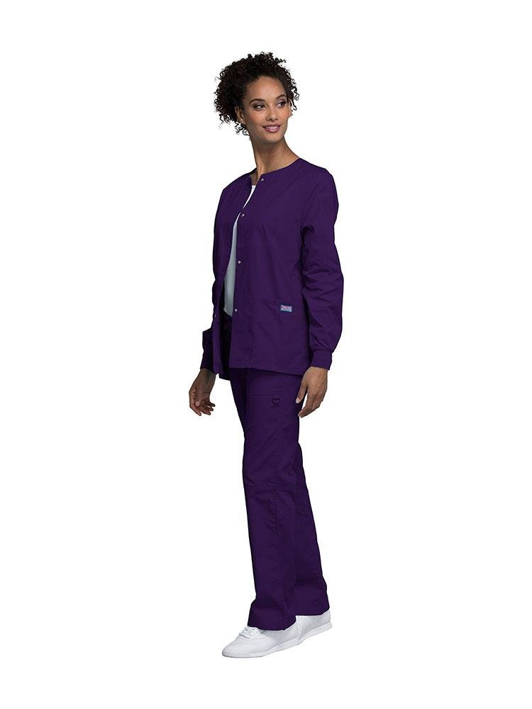 A young female Dental Assistant wearing a Cherokee Workwear Originals women's Snap Front Warm-Up Jacket in eggplant size extra small featuring a total of 3 pockets.