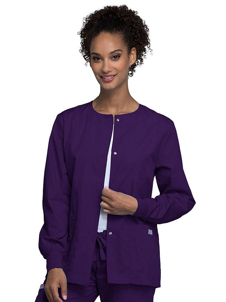 A young female Nurse wearing a Cherokee Workwear Originals Women's Snap Front Warm-Up Jacket in eggplant featuring Cotton Poplin with Soil Release.