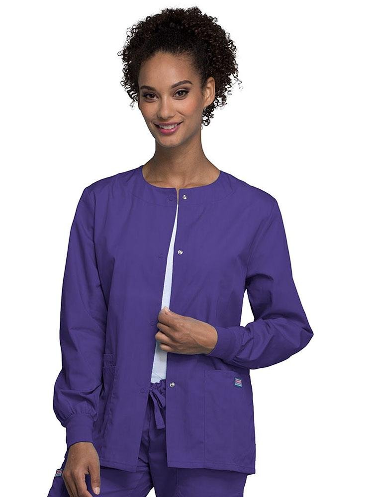 A young female Radiologic Technologist wearing a Cherokee Workwear Originals Women's Snap Front Warm-Up Jacket in grape featuring a total of 3 pockets.