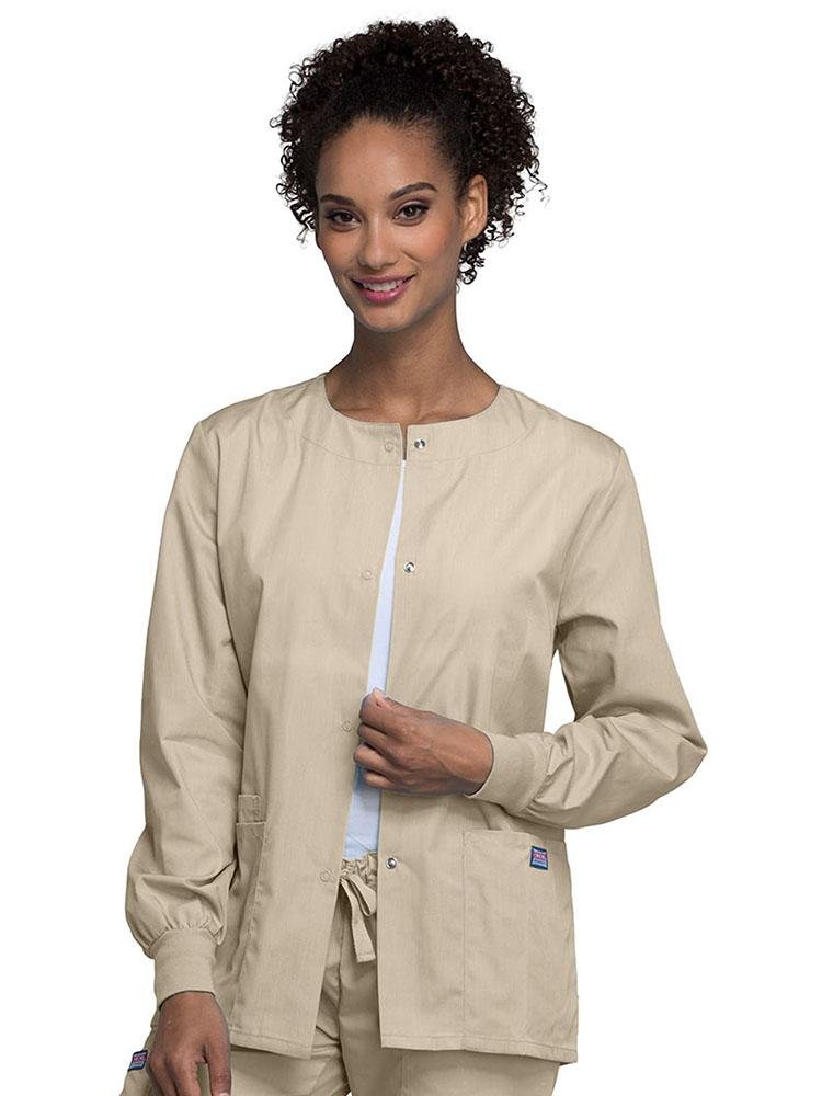A young female LPN wearing a Cherokee Workwear Originals Women's Snap Front Warm-Up Jacket in Khaki featuring A Traditional Classic fit & a round neck.