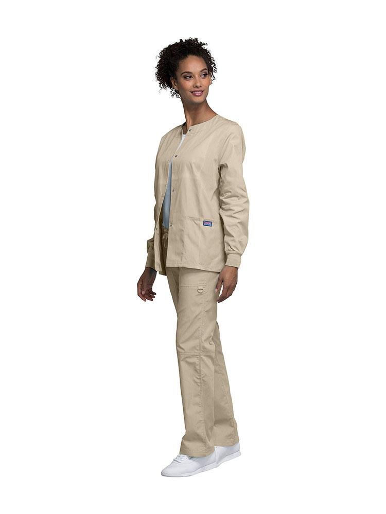 A young lady Medical Secretary wearing Cherokee Workwear Originals women's Snap Front Warm-Up Jacket in Khaki size extra small featuring knit cuffs to provide a flattering all day fit.