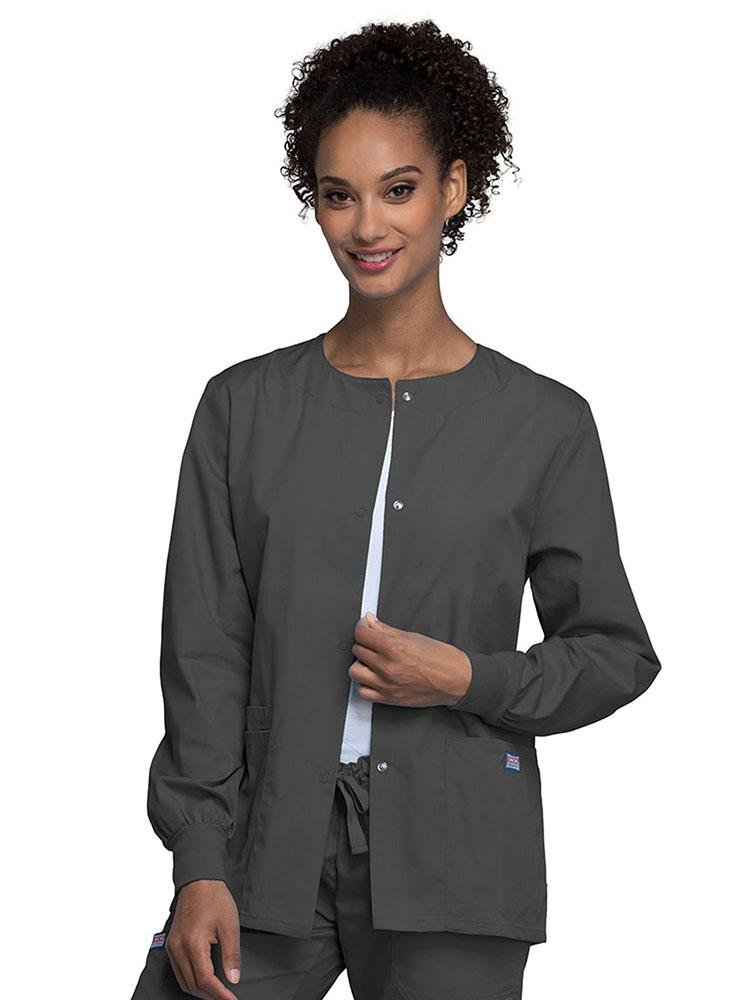 A young female Radiologic Technologist wearing a Cherokee Workwear Originals Women's Snap Front Warm-Up Jacket in Pewter featuring a total of 3 pockets.