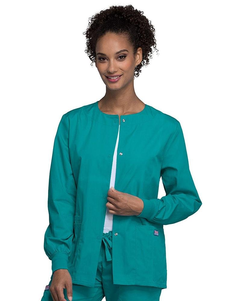 A young female LPN wearing a Cherokee Workwear Originals Women's Snap Front Warm-Up Jacket in Teal featuring A Traditional Classic fit & a round neck.