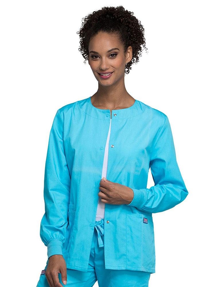 A young female Radiologic Technologist wearing a Cherokee Workwear Originals Women's Snap Front Warm-Up Jacket in Turquoise featuring a total of 3 pockets.