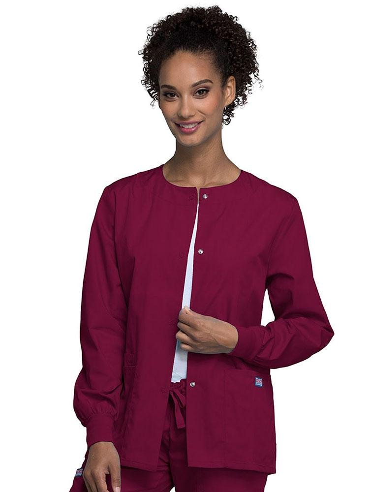 A young female Radiologic Technologist wearing a Cherokee Workwear Originals Women's Snap Front Warm-Up Jacket in wine featuring a total of 3 pockets.
