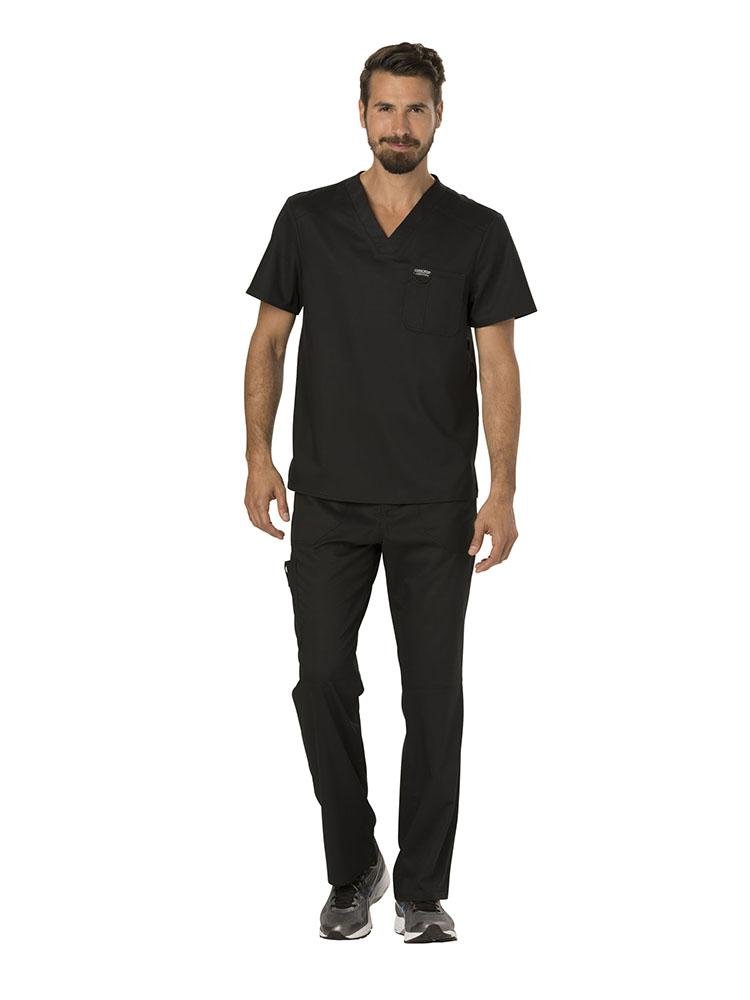A young male Pharmacy Technician wearing a Cherokee Workwear Revolution Men's Single Pocket V-neck Scrub Top in Black size Small featuring a v-neckline & short sleeves.