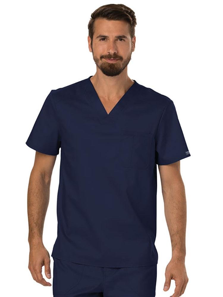 A young male Physician wearing a Cherokee Workwear Revolution Men's Single Pocket V-neck Scrub Top in Navy size XL featuring a single chest pocket on the wearer's left side.