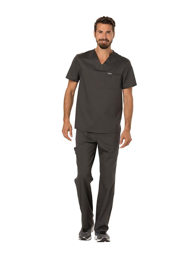 A young male Pharmacy Technician wearing a Cherokee Workwear Revolution Men's Single Pocket V-neck Scrub Top in Pewter size Medium featuring a v-neckline & short sleeves.