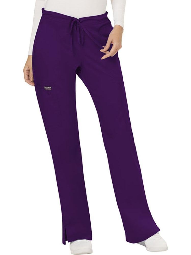 A young female CNA wearing a Cherokee Workwear Revolution Women's Mid Rise Moderate Flare Scrub Pant in Eggplant size XL Petite featuring a drawstring waist to provide a flattering & comfortable all day fit.