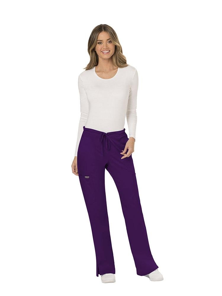 A female Dental Assistant wearing a Cherokee Workwear Revolution Women's Mid Rise Moderate Flare Scrub Pant in Eggplant size Large featuring a unique poly/spandex/rayon blend.