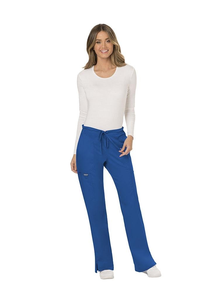 A female Nursing Assistant wearing a Cherokee Workwear Revolution Women's Mid Rise Moderate Flare Scrub Pant in Royal Blue size Large featuring a unique poly/spandex/rayon blend.
