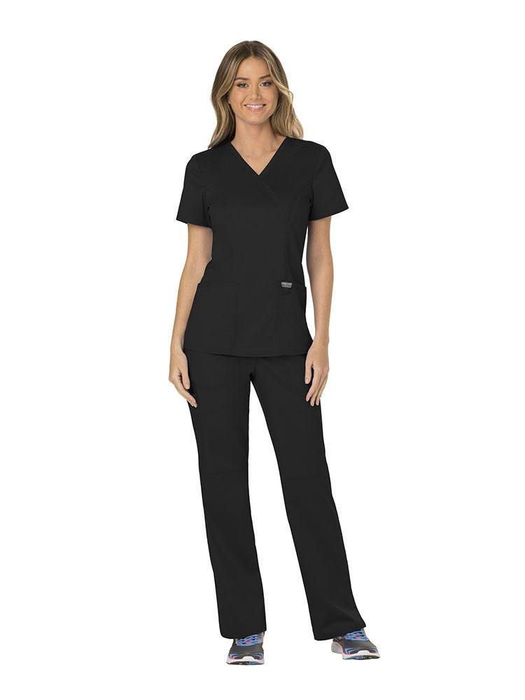 A female RN wearing a Cherokee Workwear Revolution Women's Mock Wrap Scrub Top & Elastic Waist Scrub Pant in black size extra small featuring front shoulder yokes to ensure a flattering all day fit.