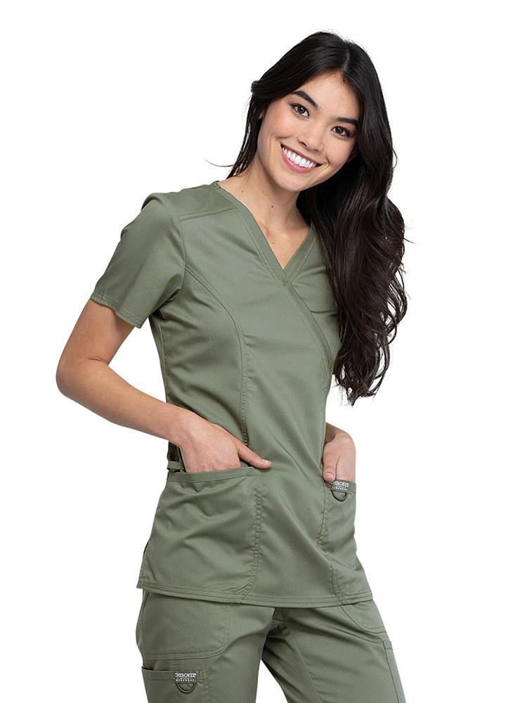 Right side view of Occupational Therapist wearing Cherokee Workwear Revolution women's Mock Wrap Scrub Top in olive size large