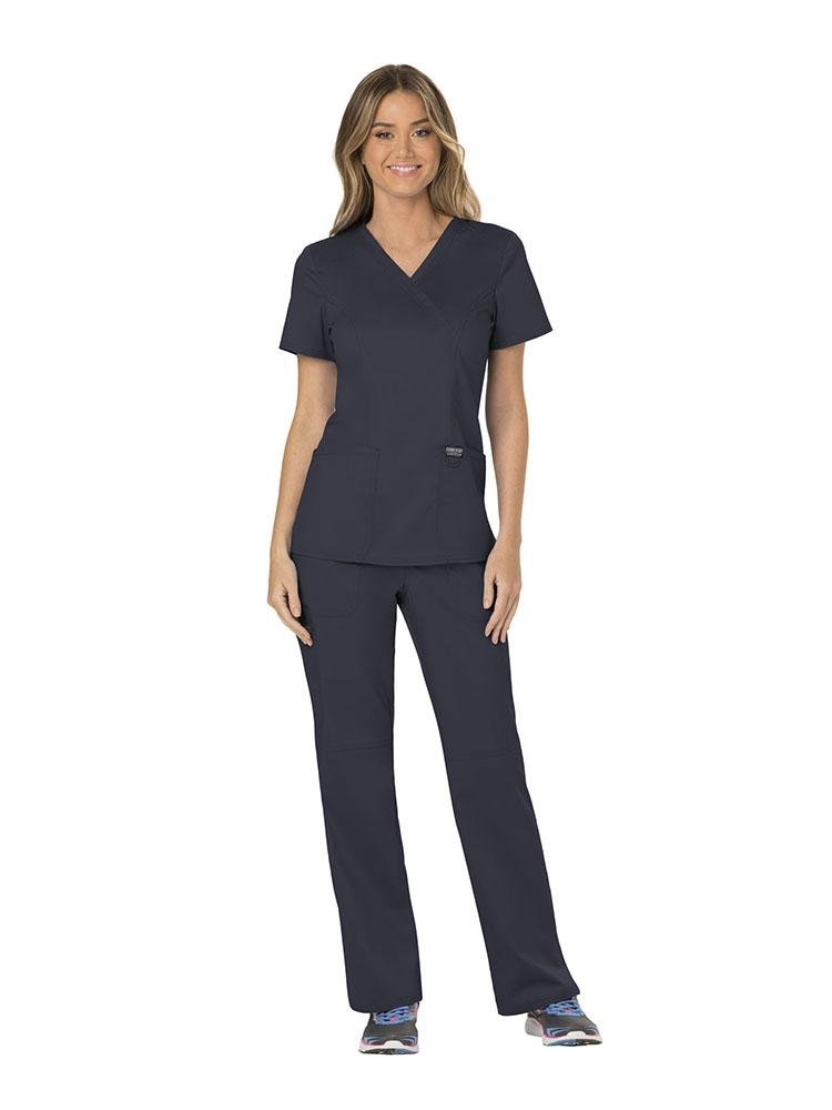 A female Home Health Aide wearing a Cherokee Workwear Revolution Women's Mock Wrap Scrub Top in Pewter size Large featuring featuring princess seams throughout to ensure a flattering all day fit.
