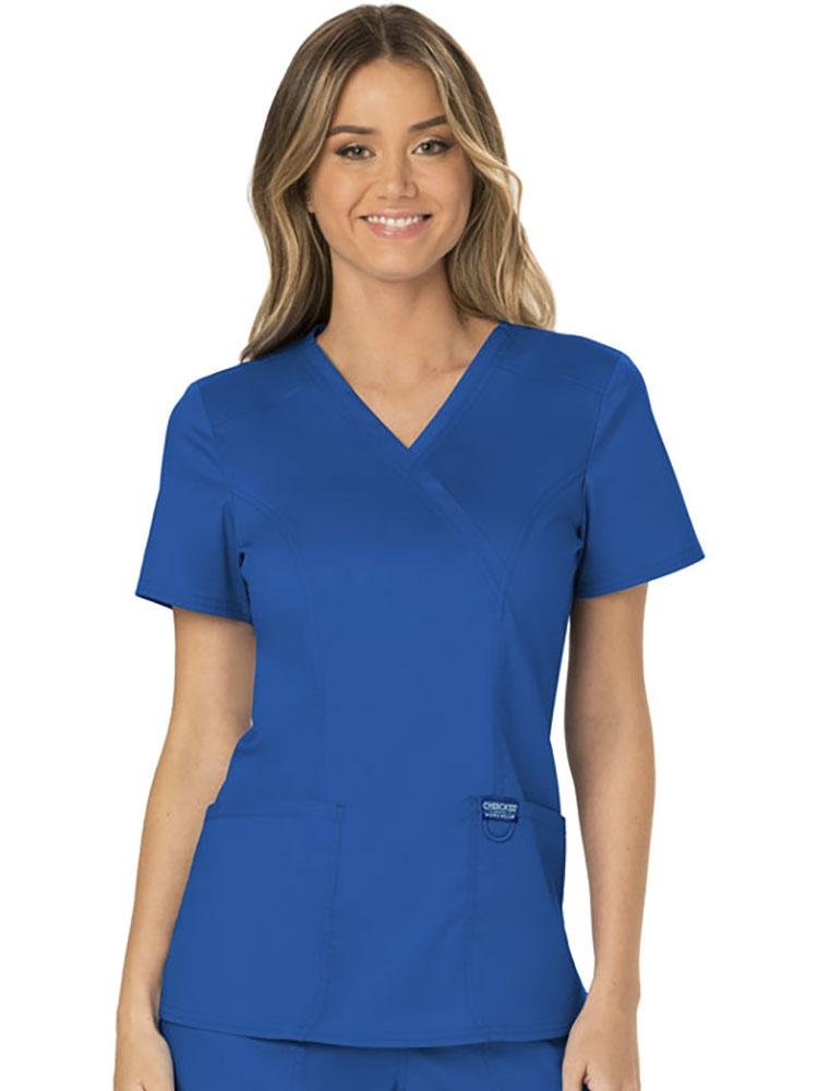 A female Physician wearing a Cherokee Workwear Revolution Women's Mock Wrap Scrub Top in Royal Blue size extra large featuring a modern classic fit with short sleeves.