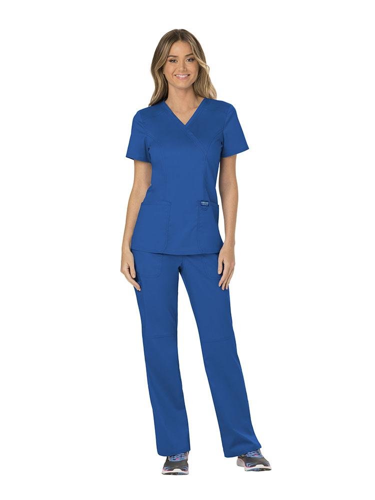 A female RN wearing a Cherokee Workwear Revolution Women's Mock Wrap Scrub Top & Elastic Waist Scrub Pant in Royal Blue size extra small featuring front shoulder yokes to ensure a flattering all day fit.