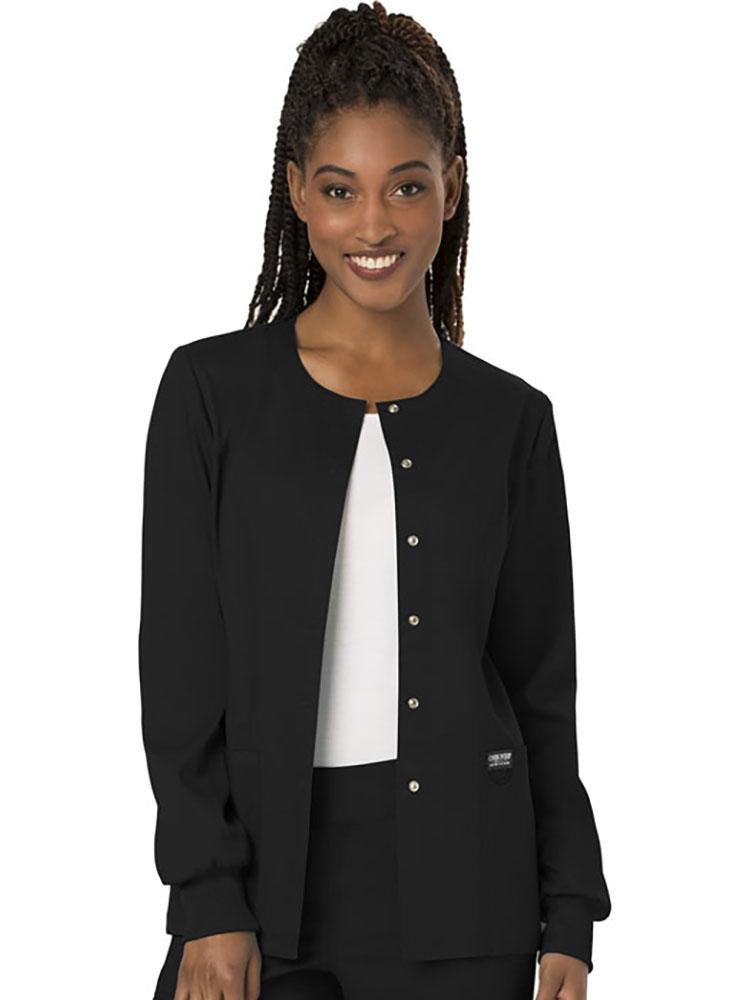 A young female Medical Assistant wearing a Cherokee Workwear Revolution women's Snap Front Scrub Jacket in Black size large featuring snap front closure.