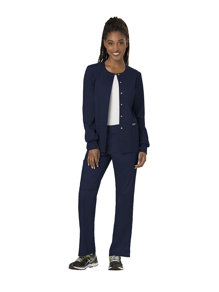 A female MRI Tech wearing a Cherokee Workwear Revolution women's Snap Front Scrub Jacket in Navy size extra small featuring 2 front patch pockets for easy storage.