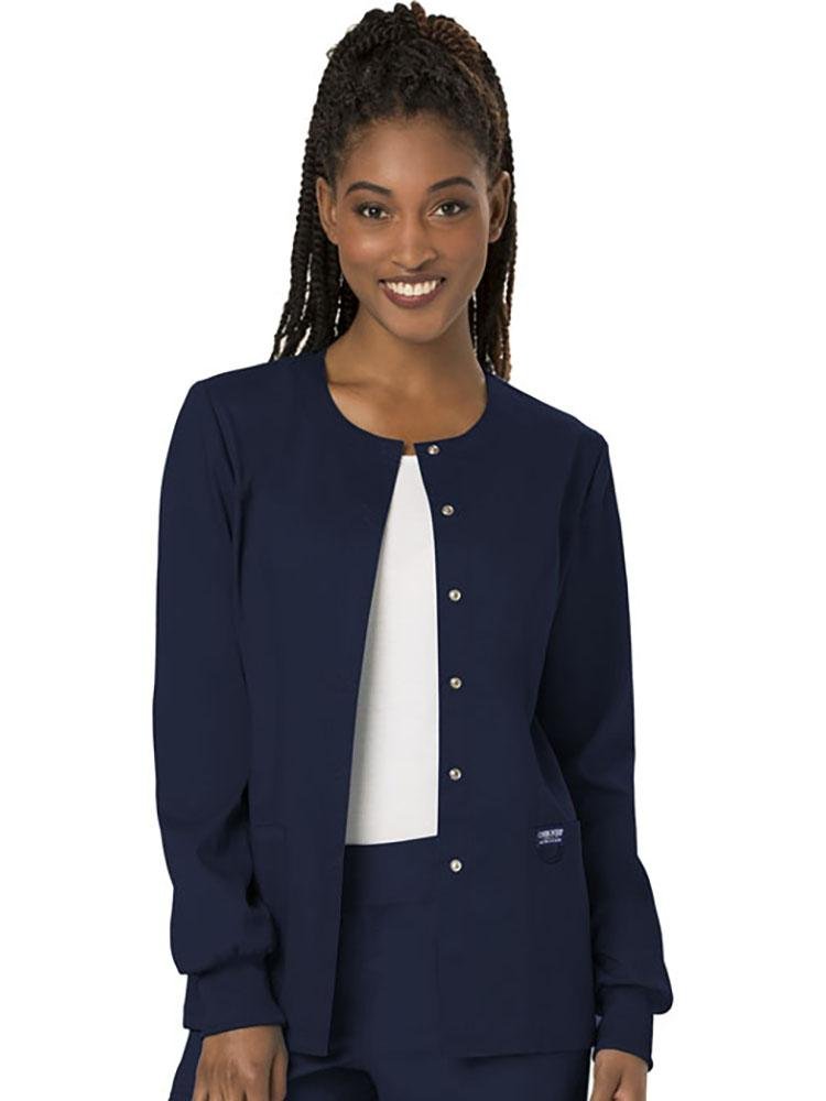 A young female Family Practitioner wearing a Cherokee Workwear Revolution women's Snap Front Scrub Jacket in Navy size large featuring snap front closure.