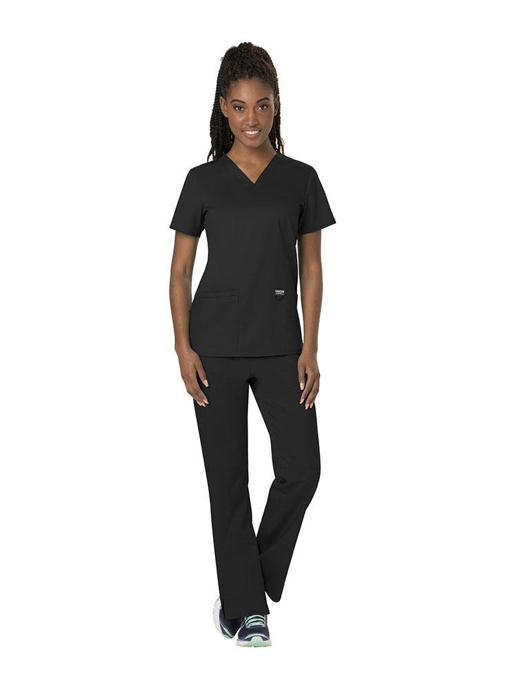 A young female Nurse wearing both the Cherokee Workwear Revolution women's V-Neck Scrub Top & Elastic Waistband Pull-On Scrub Pant in black size extra small.