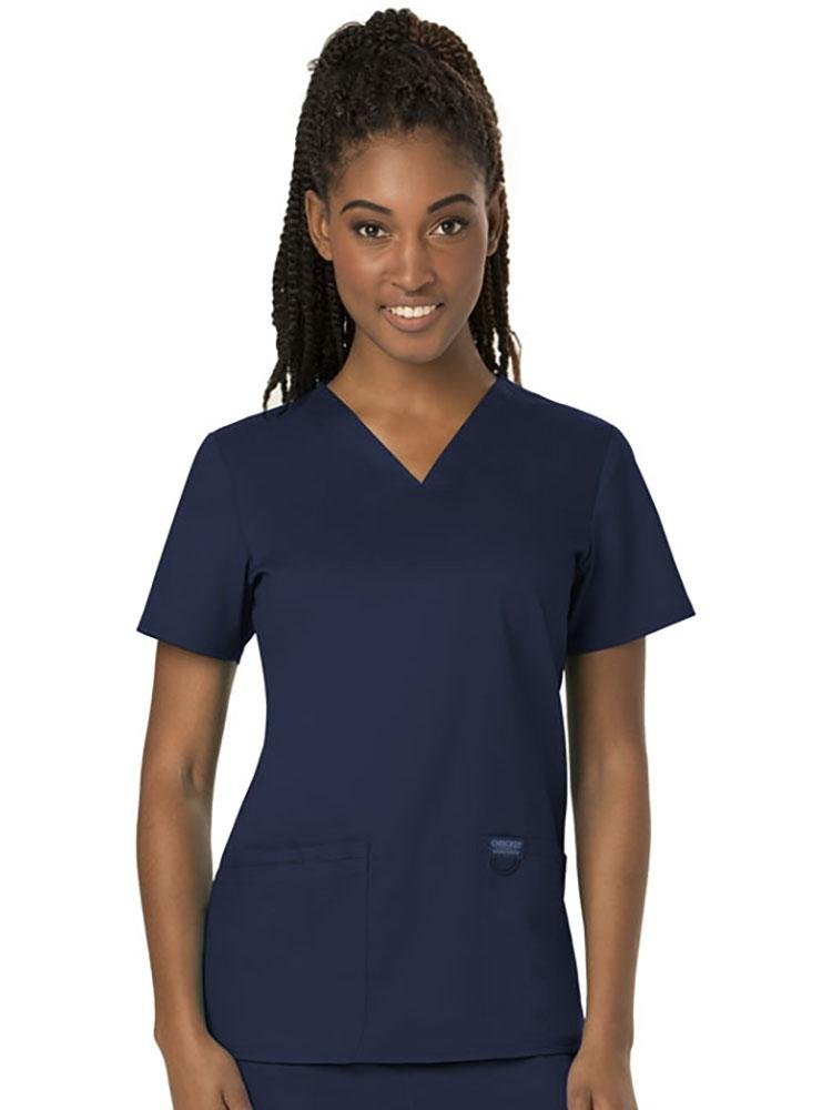A young female LPN wearing a Cherokee Women's Revolution Women's V-neck Scrub Top in Navy size Small featuring 2 front pockets for you on the job storage needs.