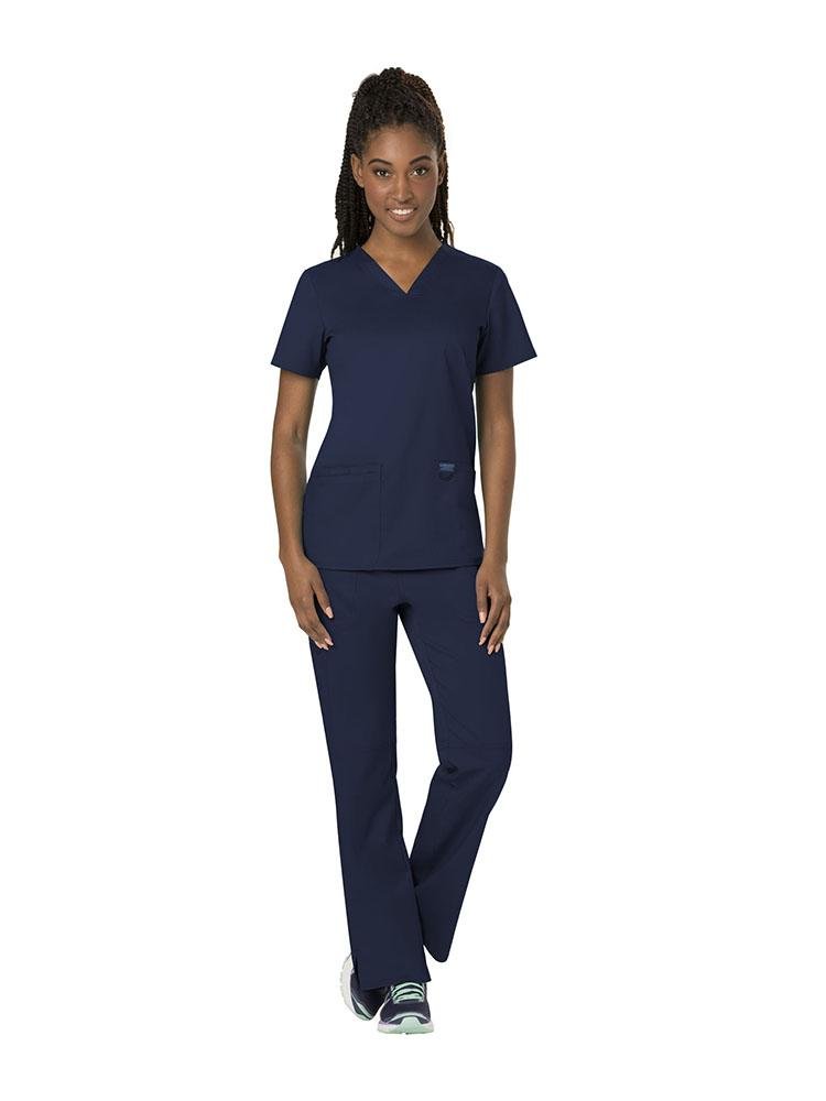 A young female Physician wearing both the Cherokee Workwear Revolution women's V-Neck Scrub Top & Elastic Waistband Pull-On Scrub Pant in Navy size XL.