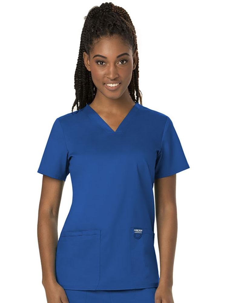 A young female Dermatologist  wearing a Cherokee Women's Revolution Women's V-neck Scrub Top in Royal size 4XL featuring 2 front pockets for you on the job storage needs.