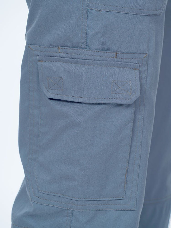 Man wearing an Epic by MedWorks Men's Button Front Scrub Pant in blue fog with 1 double cargo pocket on wearer's right side.