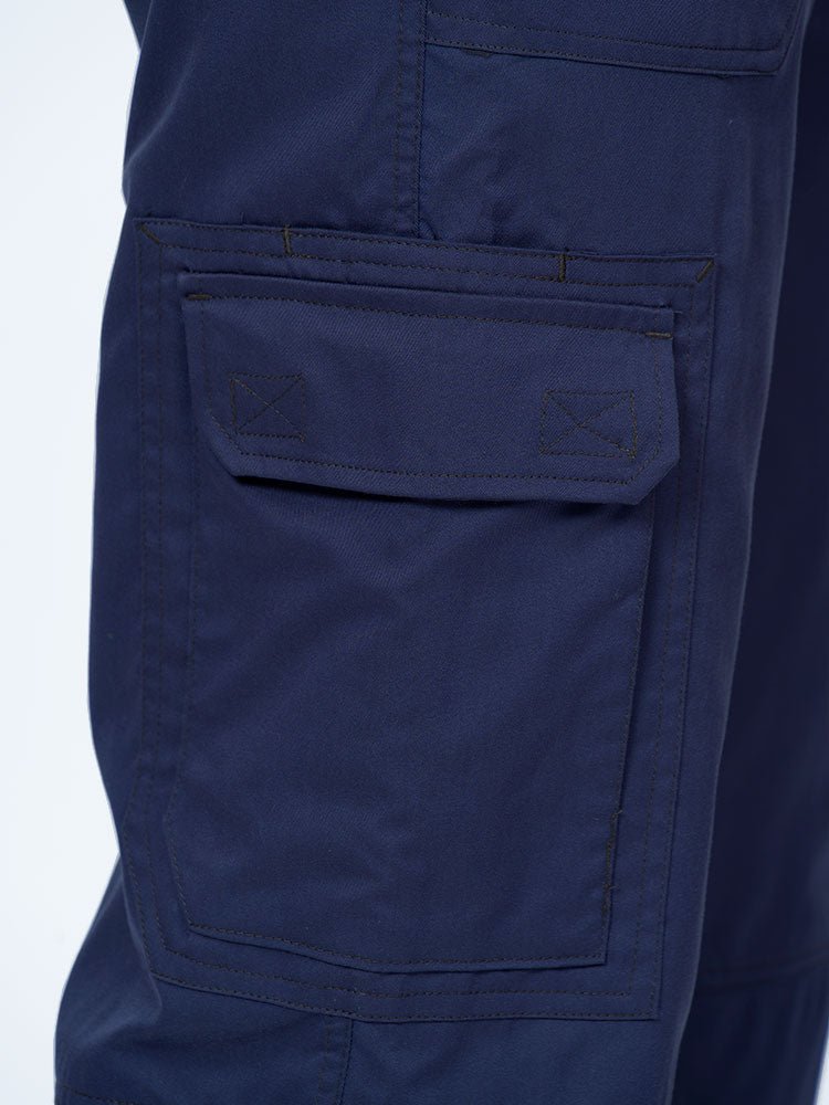 Man wearing an Epic by MedWorks Men's Button Front Scrub Pant in navy with 1 double cargo pocket on wearer's right side.