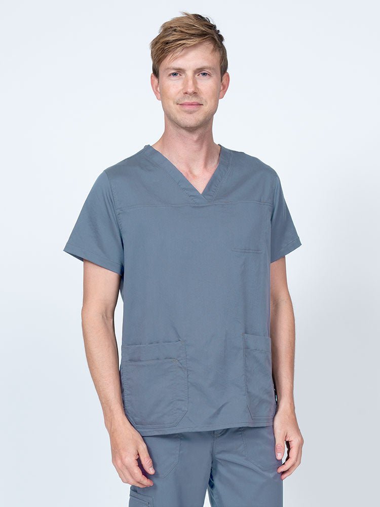 Male healthcare professional wearing an Epic by MedWorks Men's Scrub Top in blue fog with 2 front patch pockets and 1 exterior cell phone pocket on the wearer's right side.