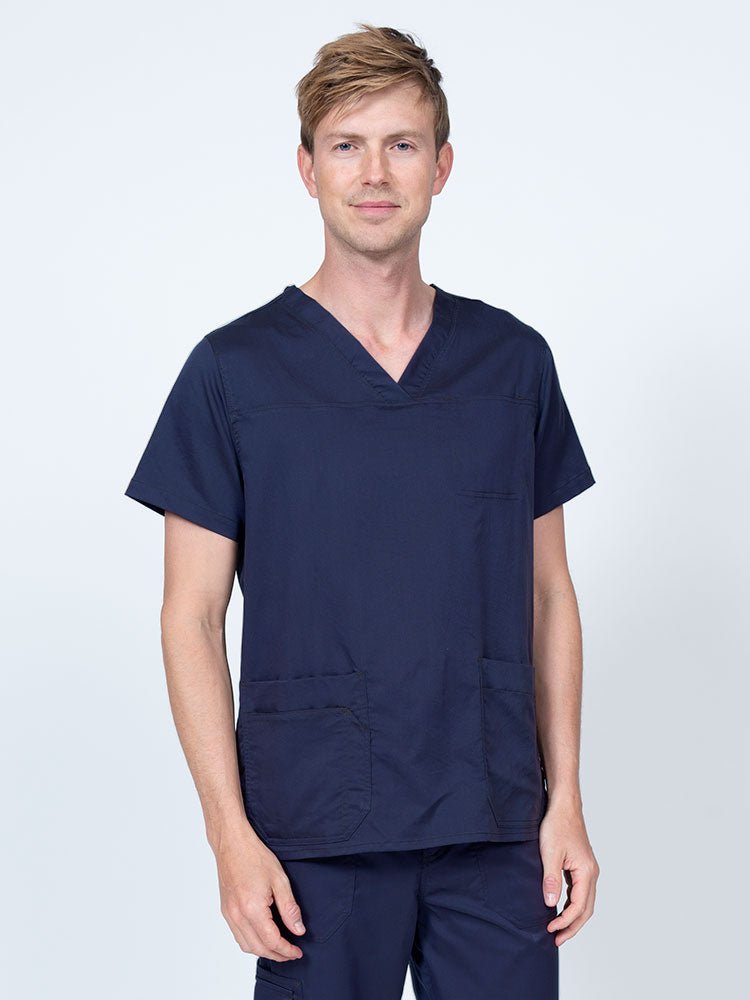 Male healthcare professional wearing an Epic by MedWorks Men's Scrub Top in navy with 2 front patch pockets and 1 exterior cell phone pocket on the wearer's right side.
