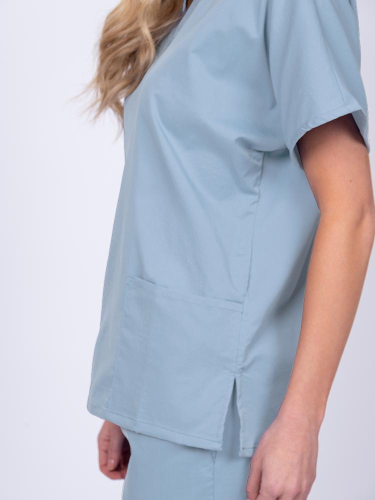 Young female healthcare worker wearing an Epic by MedWorks Unisex V-Neck Scrub Top in blue fog with side slits for mobility & flair.