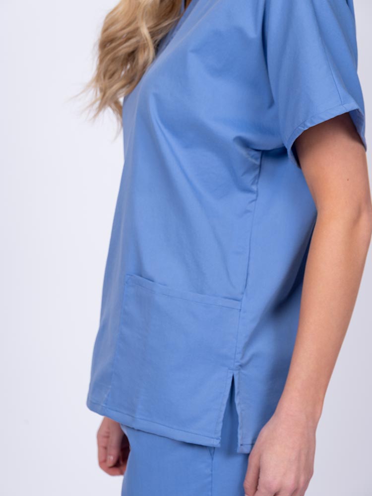 Young female healthcare worker wearing an Epic by MedWorks Unisex V-Neck Scrub Top in ceil with side slits for mobility & flair.