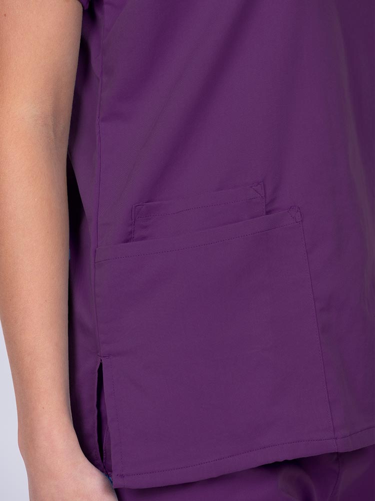 Woman wearing an Epic by MedWorks Unisex V-Neck Scrub Top in eggplant with 2 patch pockets and a cell phone pocket.