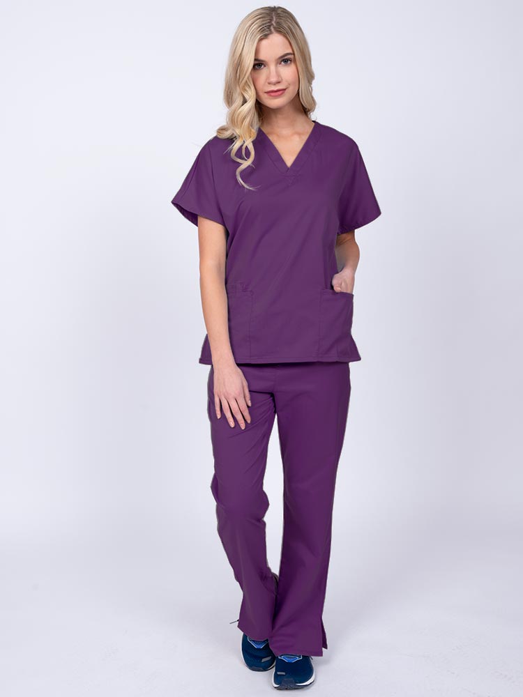 Young woman wearing an Epic by MedWorks Unisex Scrub Top in eggplant featuring a V-neckline & short sleeves.