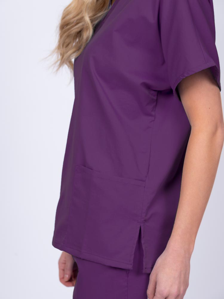 Young female healthcare worker wearing an Epic by MedWorks Unisex V-Neck Scrub Top in eggplant with side slits for mobility & flair.