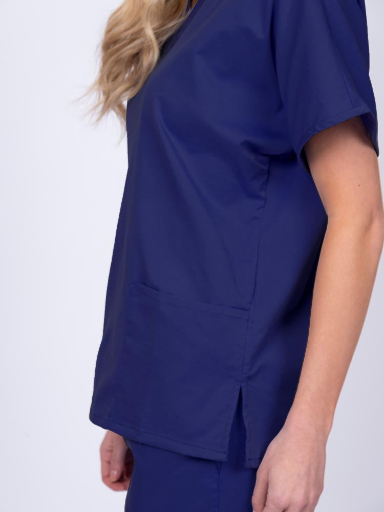 Young female healthcare worker wearing an Epic by MedWorks Unisex V-Neck Scrub Top in navy with side slits for mobility & flair.