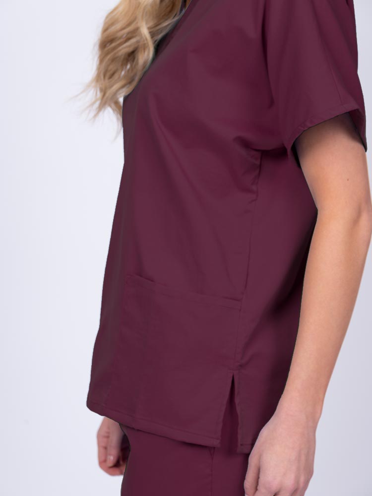 Young female healthcare worker wearing an Epic by MedWorks Unisex V-Neck Scrub Top in wine with side slits for mobility & flair.