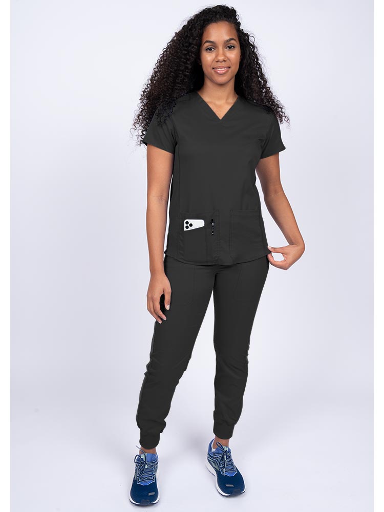Young female healthcare professional wearing an Epic by MedWorks Women's Blessed Scrub Top in black with a total of 3 pockets & 1 pen slot.