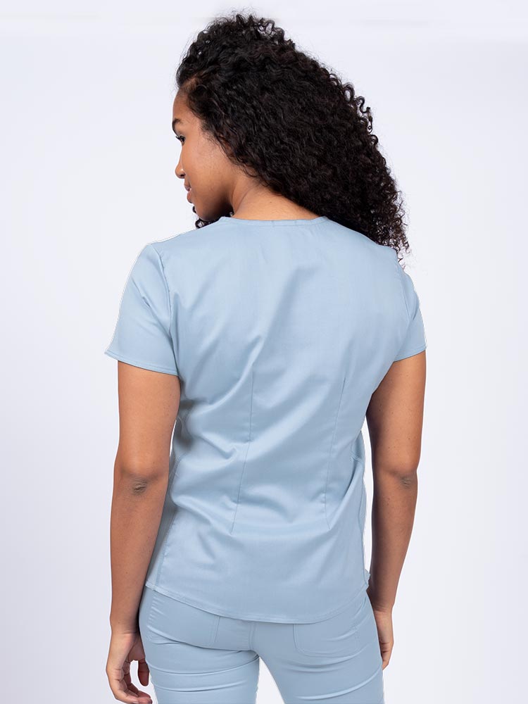 Woman wearing an Epic by MedWorks Women's Blessed Scrub Top in blue fog with a pleated back for a flattering fit.