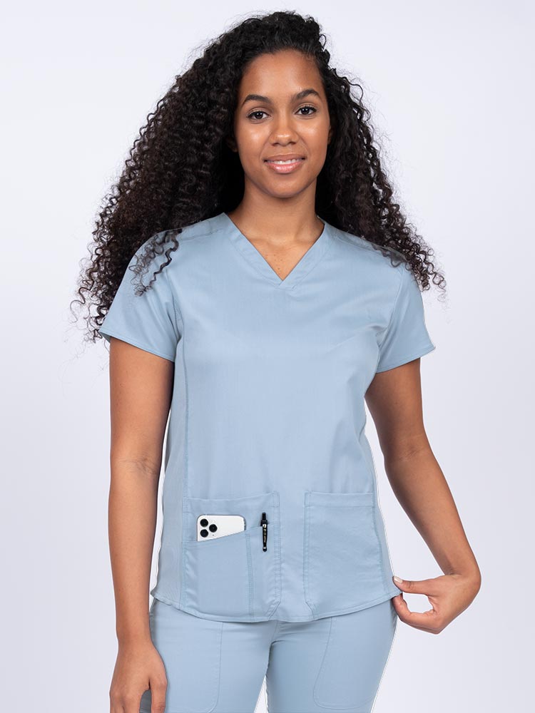 Nurse wearing an Epic by MedWorks Women's Blessed Scrub Top in blue fog with a V-neckline & short sleeves.