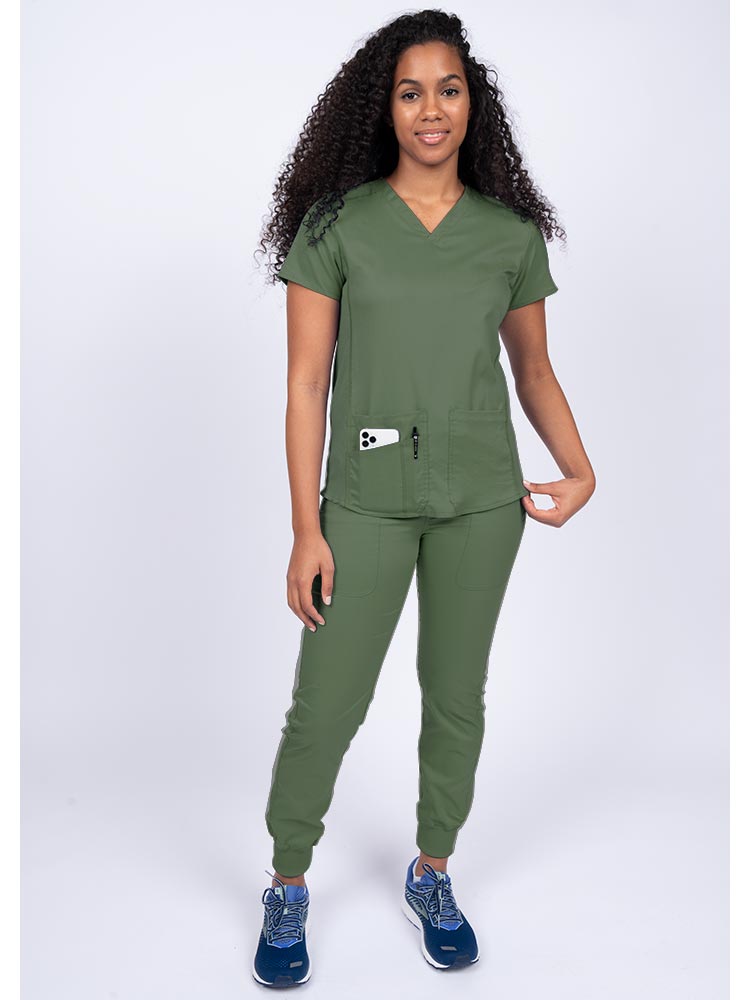 Young female healthcare professional wearing an Epic by MedWorks Women's Blessed Scrub Top in olive with a total of 3 pockets & 1 pen slot.