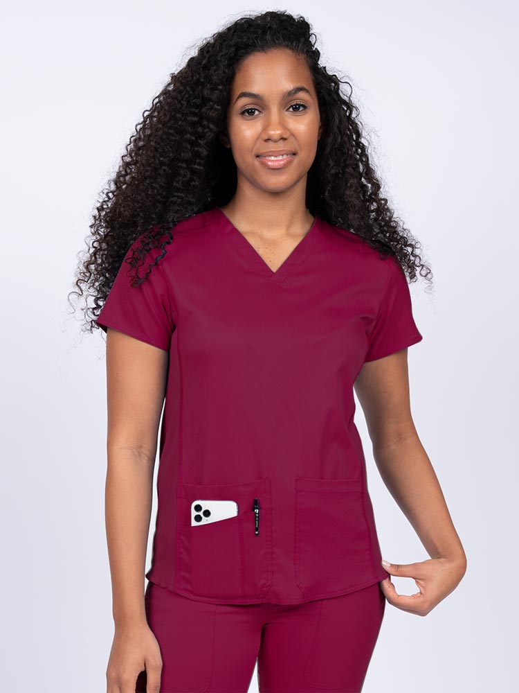 Nurse wearing an Epic by MedWorks Women's Blessed Scrub Top in wine with a V-neckline & short sleeves.
