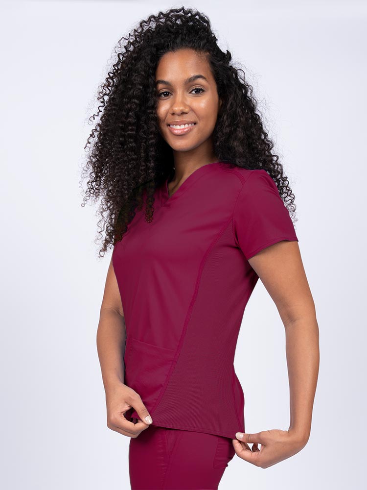 Woman wearing an Epic by MedWorks Women's Blessed Scrub Top in wine with a pleated back for a flattering fit.