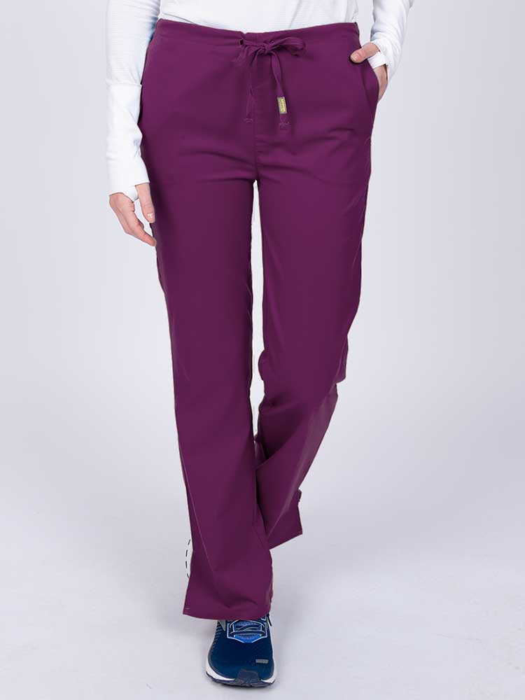 Young nurse wearing an Epic by MedWorks Women's Drawstring Flare Leg Scrub Pant in eggplant with unique stretch fabric made of 77% Polyester, 21% Viscose, 2% Spandex.