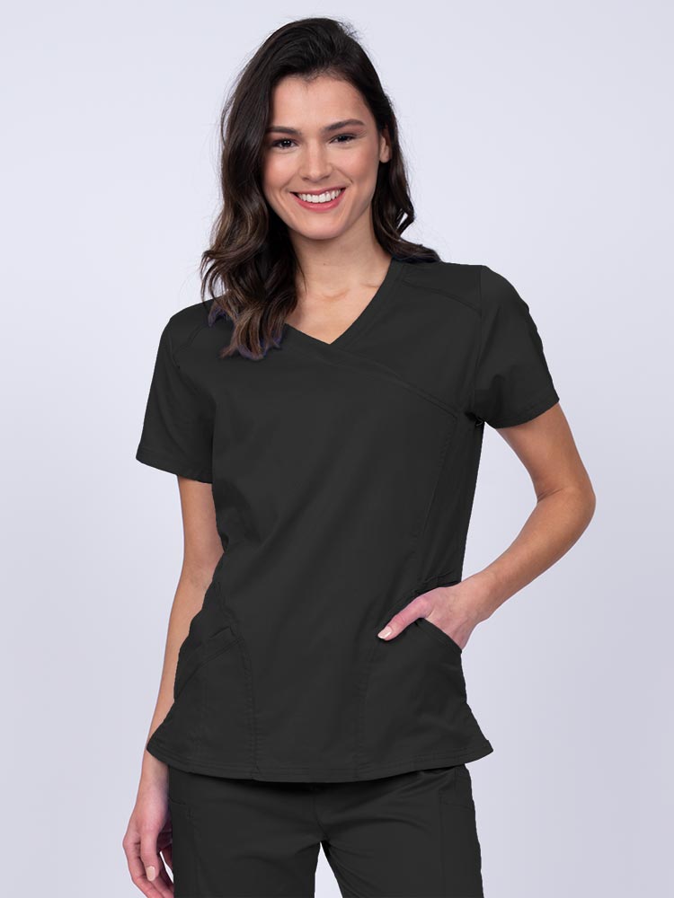 Young RN wearing an Epic by MedWorks Women's Knit Collar Mock Wrap Scrub Top in black featuring a Y-neckline with short sleeves.