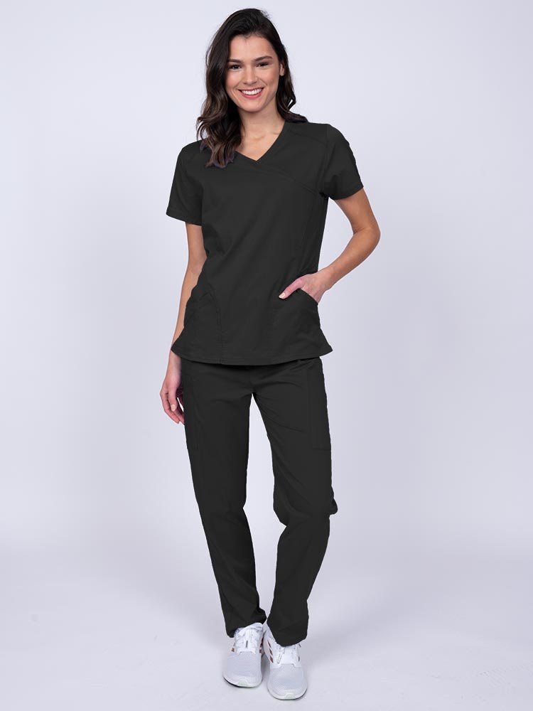 Young female healthcare worker wearing an Epic by MedWorks Women's Knit Collar Mock Wrap Scrub Top in black featuring a 2 way stretch fabric that allows air to pass easily through the garment.